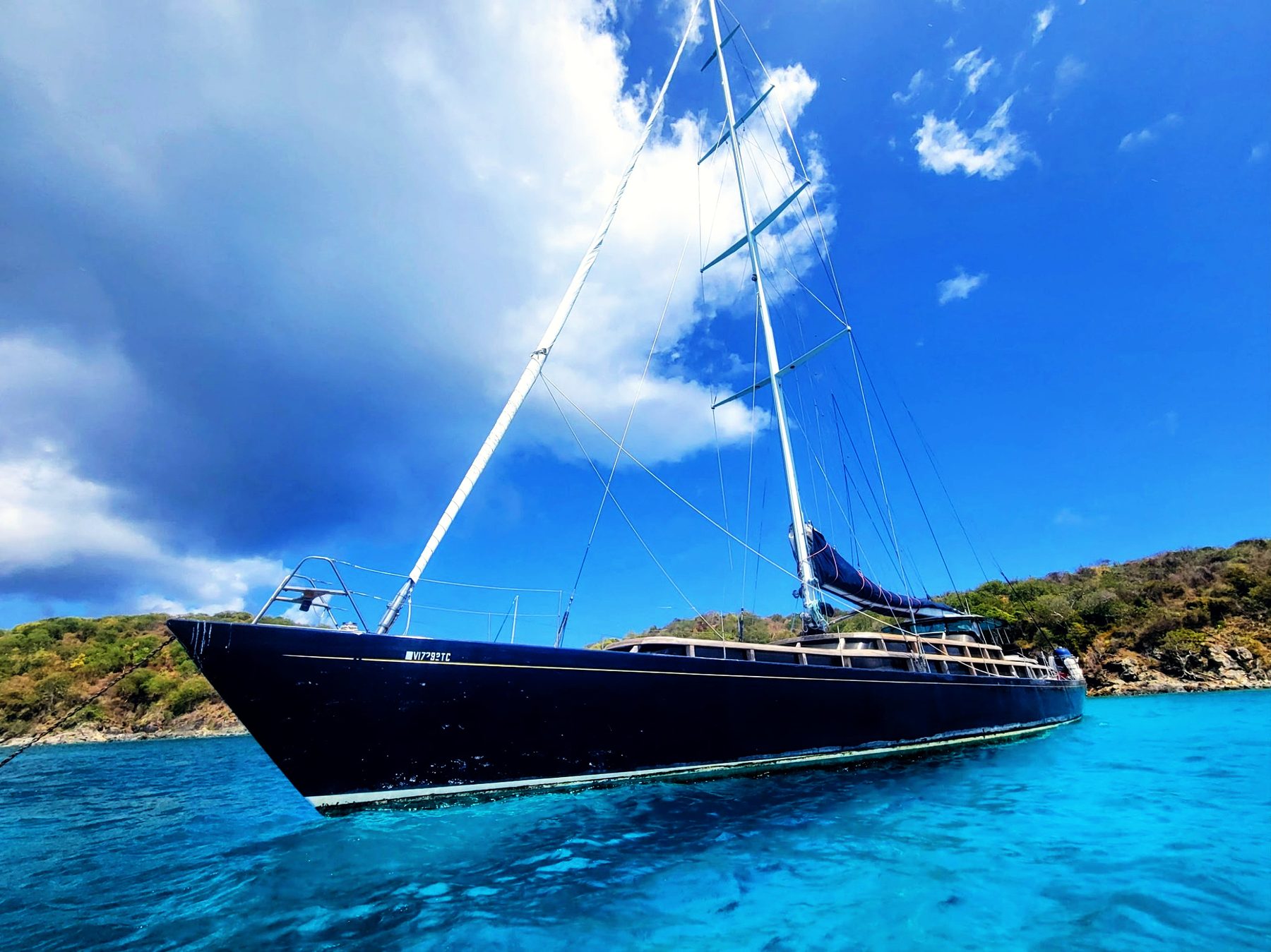 Lauren L at anchor, dark hull against turquoise water and a bank of cloud
