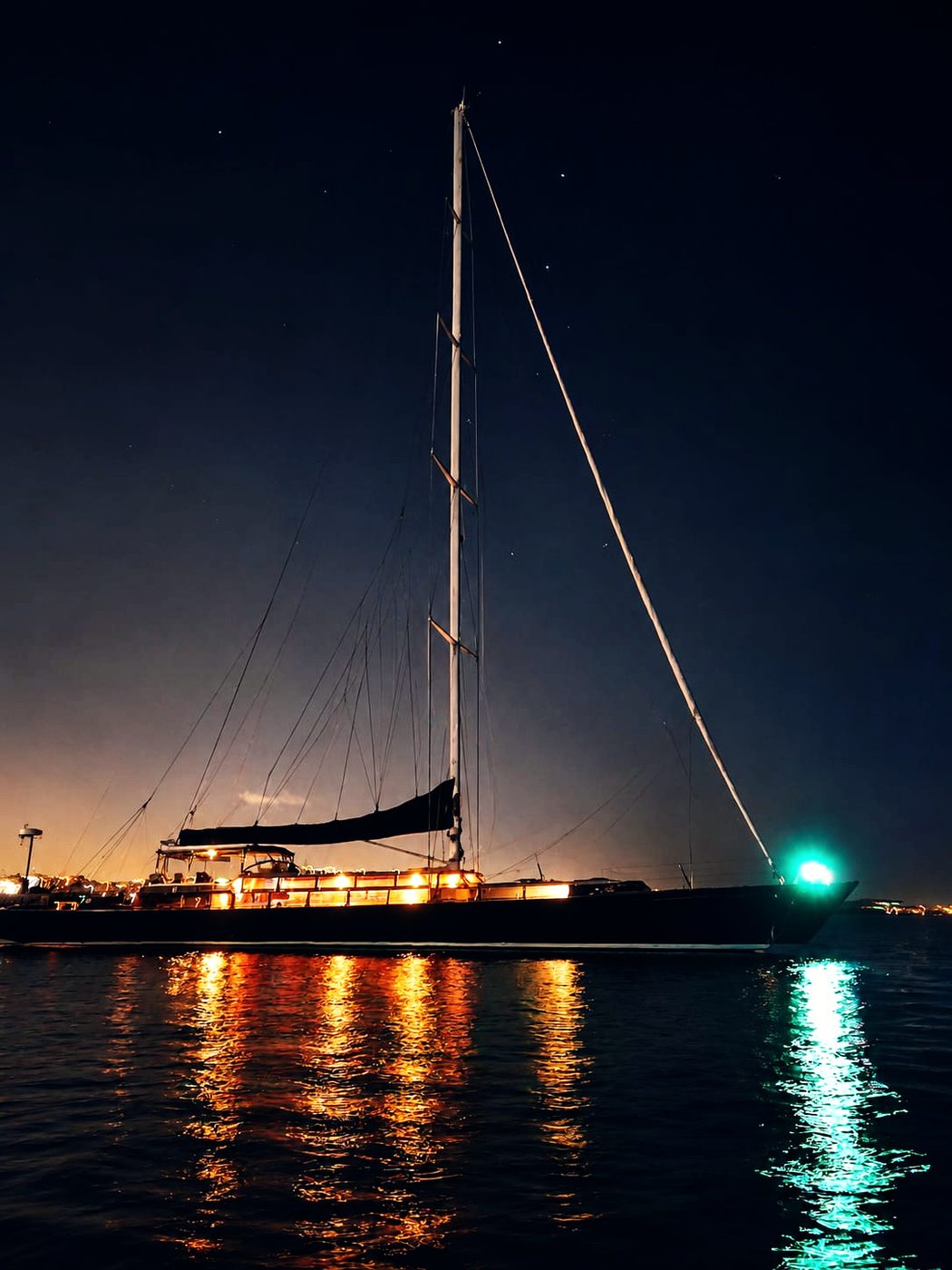 Lauren L lit at anchor after dark, her lights and starboard light reflected across the water