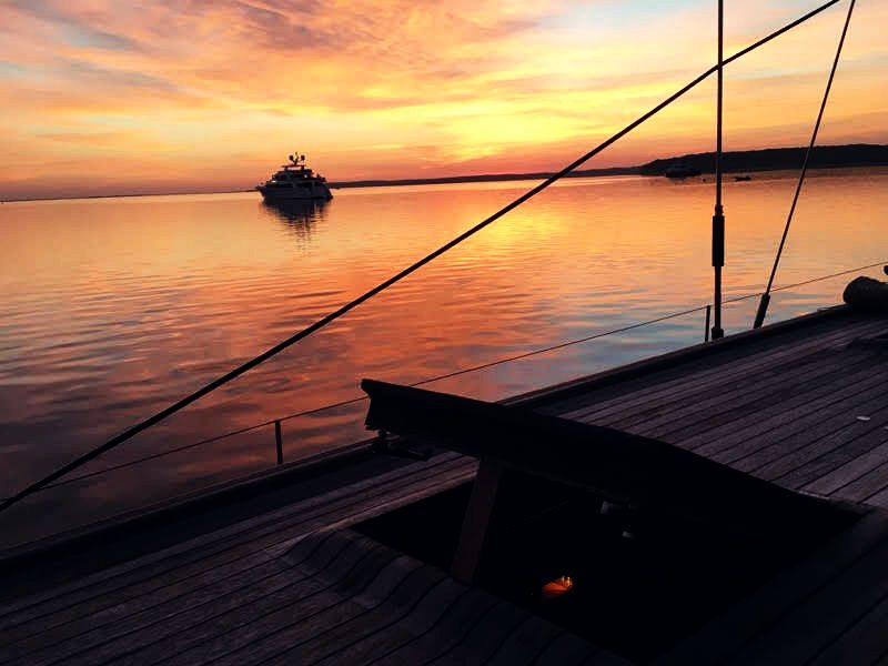 Sunset seen across the side deck, another yacht at anchor in the distance